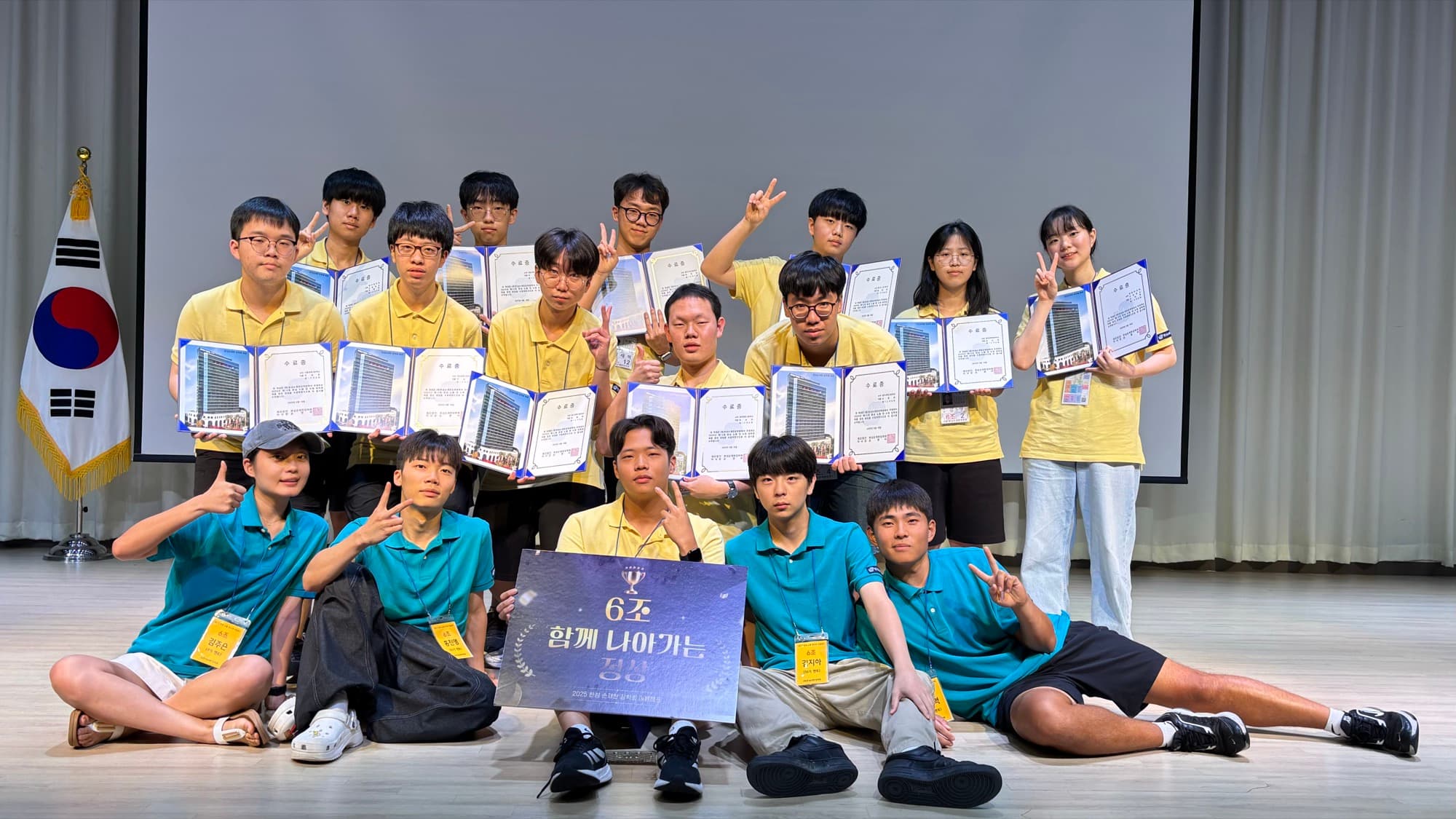 Camp participants on stage holding certificates at a "6기 함께 나아가는 여름" (6th cohort, summer) ceremony, wearing yellow and teal shirts.