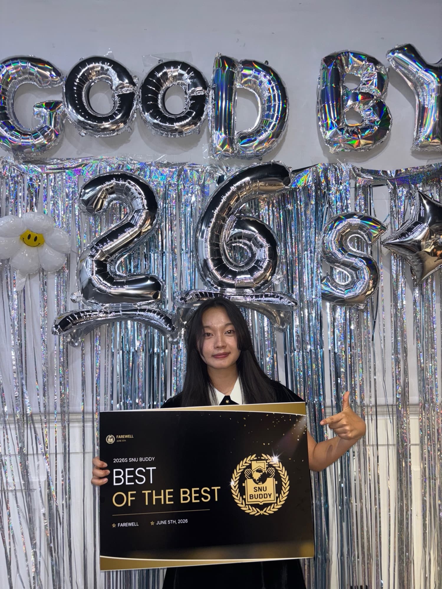 Nicole holding a black-and-gold "Best of the Best" SNU Buddy award sign in front of silver "Good Bye 26S" balloon letters at the program's farewell event.