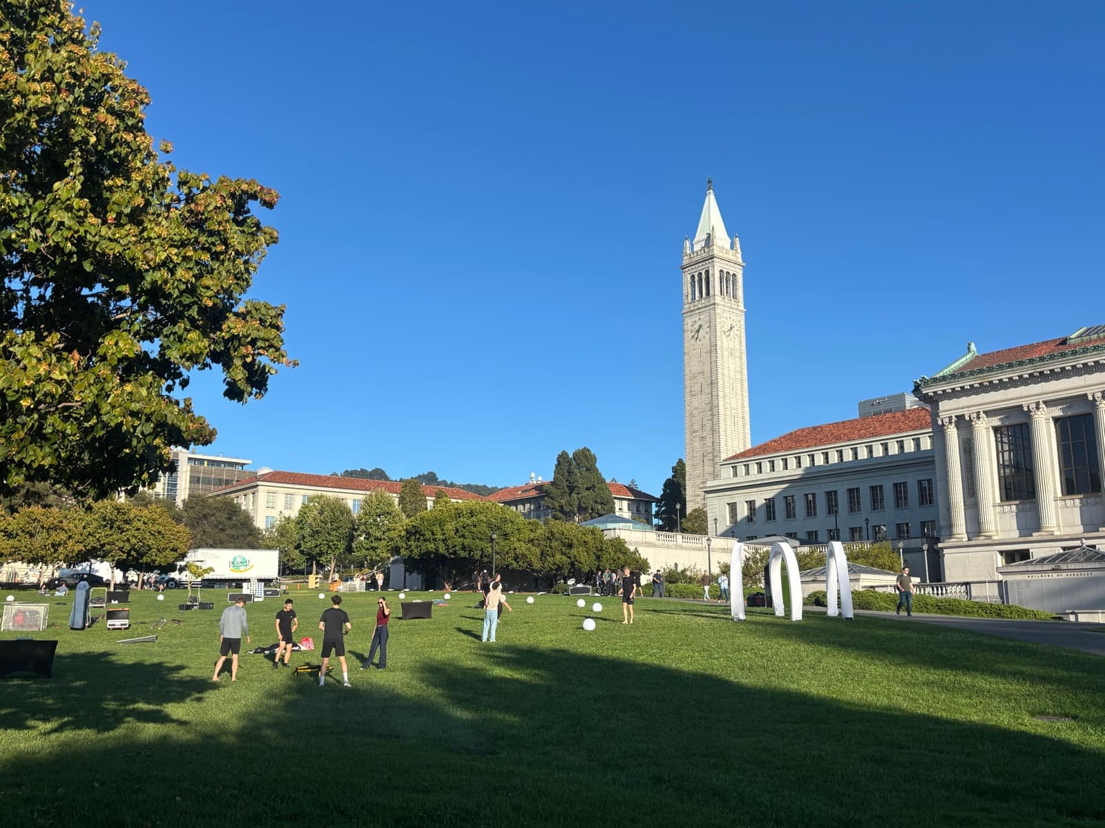 UC Berkeley's Sather Tower (the Campanile) rising above campus buildings, seen across a lawn on Memorial Glade on a clear day.