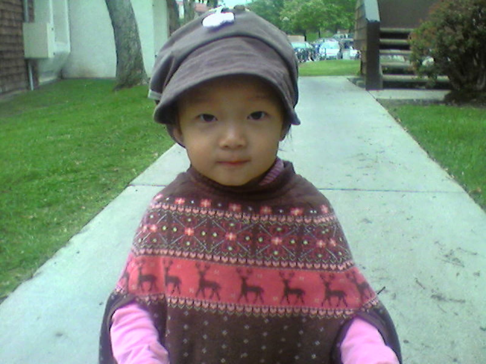 A young Nicole in a hooded jacket and reindeer-pattern sweater, standing on a sidewalk in a California neighborhood.