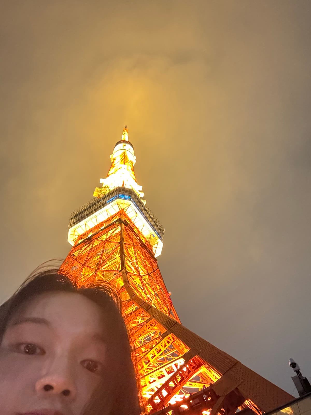 A close-up selfie of Nicole with Tokyo Tower lit up at night behind her.