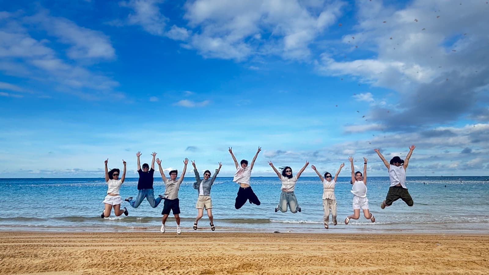 Nicole and a group of friends jumping in the air together on a beach, with the ocean behind them.