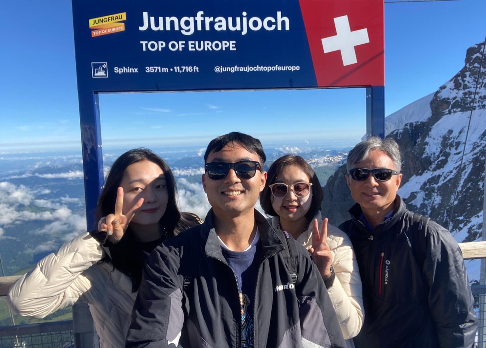 Nicole and family members smiling and making peace signs in front of the "Jungfraujoch — Top of Europe" sign, with snow-capped Swiss Alps behind them.